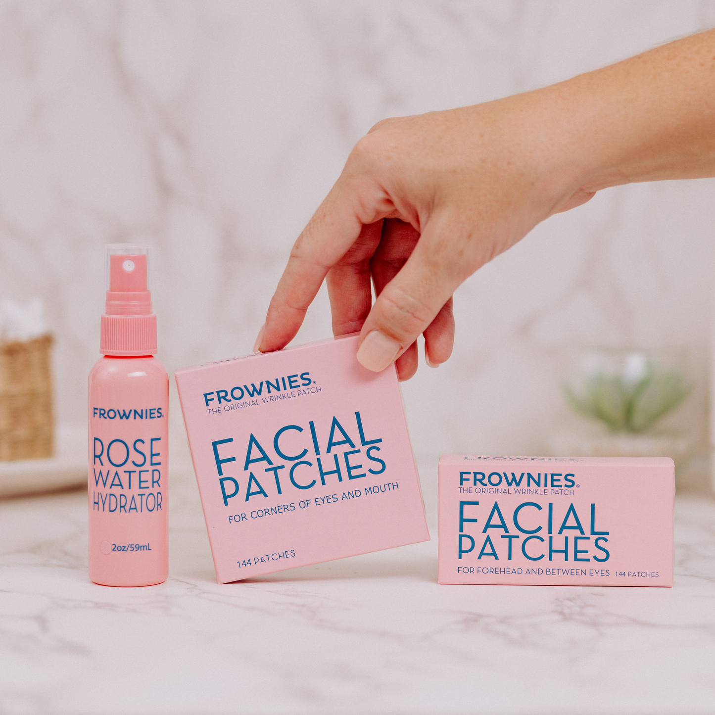 Hand som plockar upp Frownies Facial Patches-förpackning ur Startkit med Rose Water Hydrator.