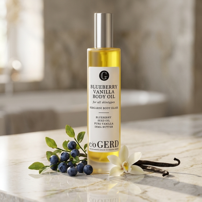 Blueberry Vanilla Body Oil i gul glasflaska på marmorbord med blåbär, vaniljstång och jasminblomma – c/o Gerd
