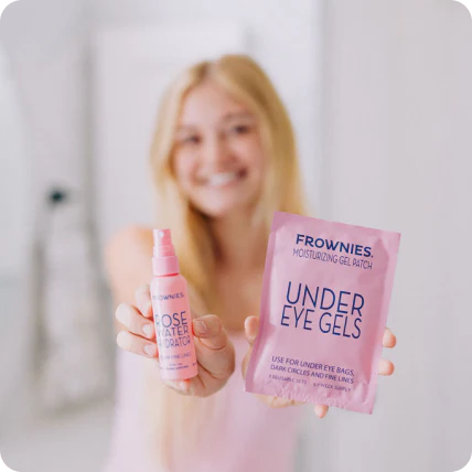 Leende blond kvinna som håller upp Frownies Under Eye Gels-förpackning i rosa toner.