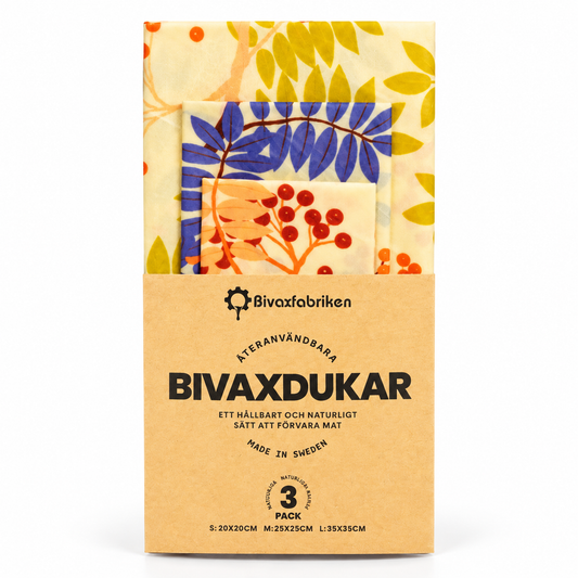 Bivaxfabriken återanvändbara bivaxdukar i tre storlekar med gula blad, blå blad och orange bär på ljus botten, i naturfärgad pappersförpackning mot vit bakgrund.