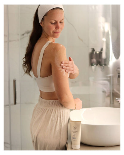 Kvinna smörjer in huden med Dr Sannas Body Lotion med lavendel och probiotika i ett ljust badrum.
