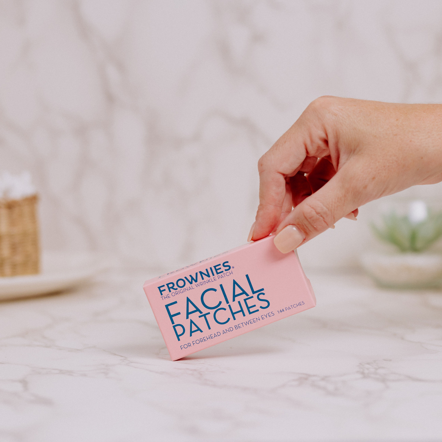 Frownies Facial Patches hålls i handen ovanför en ljus badrumsmiljö.