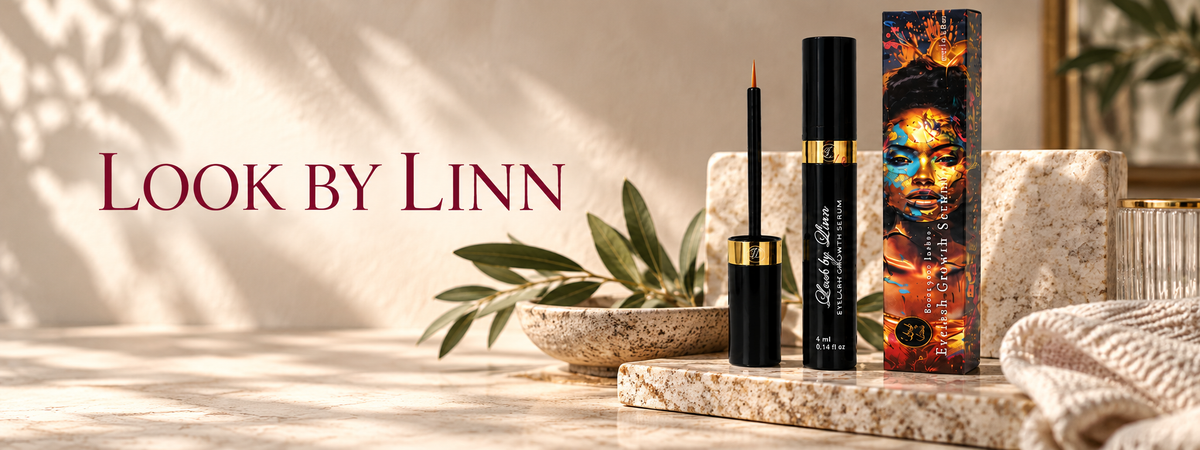 Look by Linn fransserum i svart och guld mot en varm naturfärgad bakgrund med olivblad och sten.