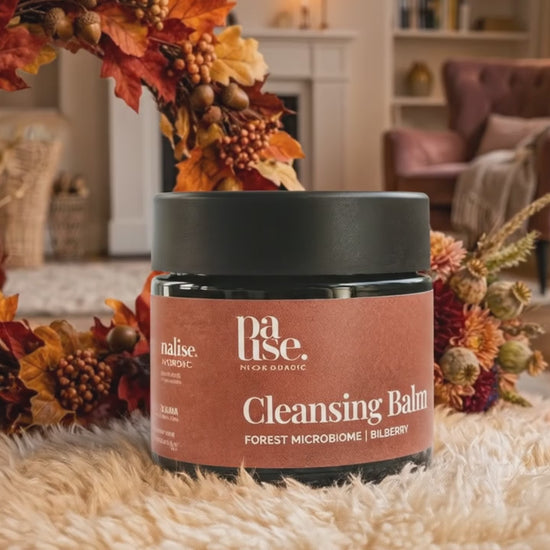 Cleansing Balm från Pause Nordic i en varm höstmiljö med brasa, höstlöv och blommor, med subtilt gnistrande ljuseffekt.
