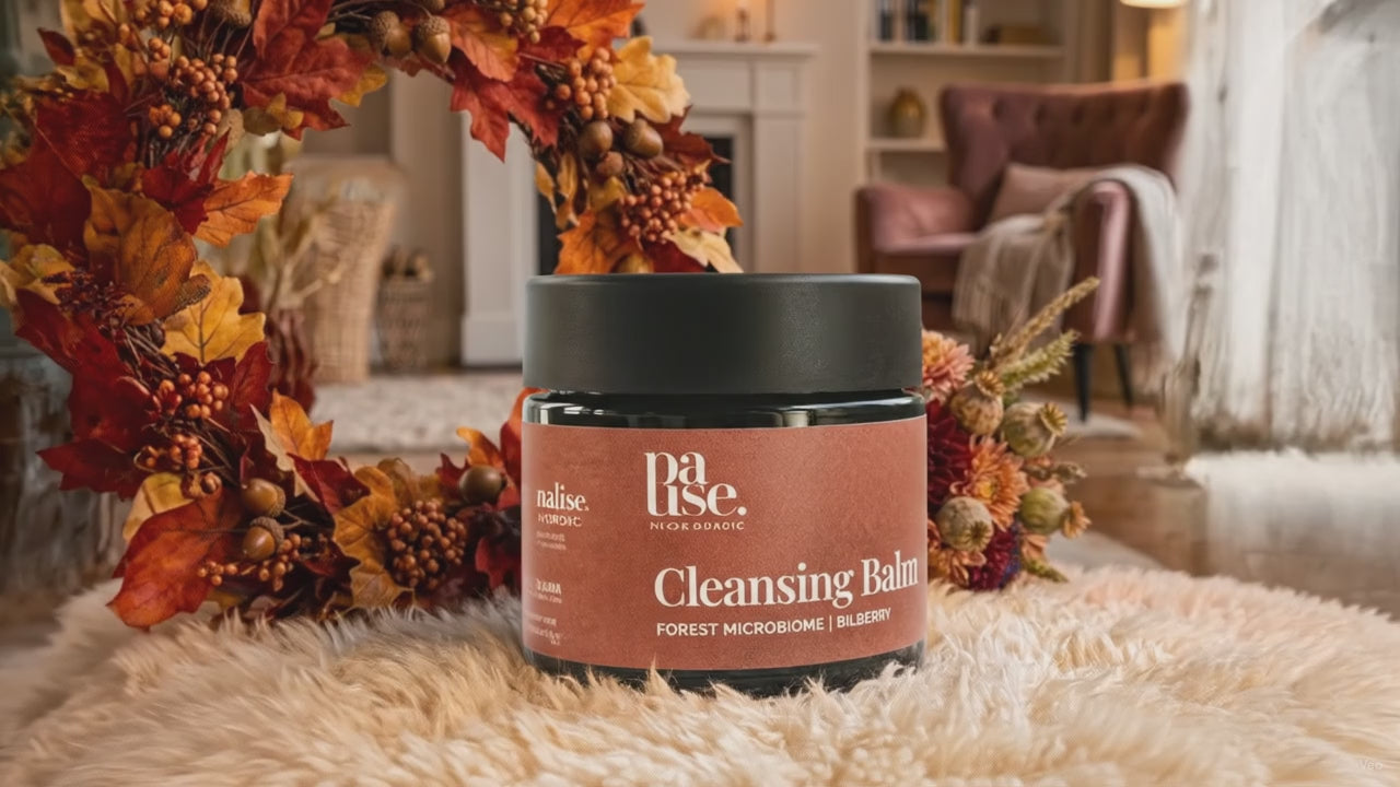 Cleansing Balm från Pause Nordic i en varm höstmiljö med brasa, höstlöv och blommor, med subtilt gnistrande ljuseffekt.